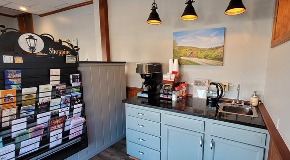A hotel reception area with a coffee machine, a counter with various items, and a wall-mounted sign. - The Canyon Motel (Wellsboro)