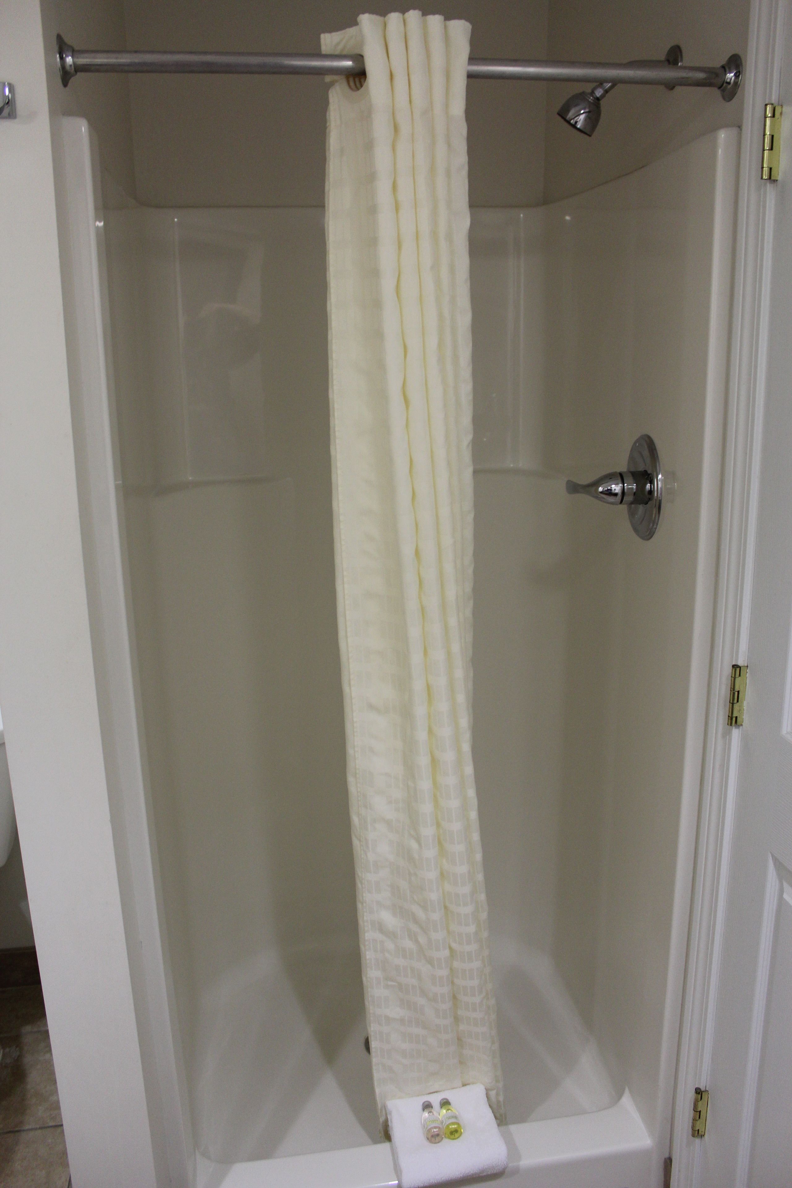 Eine Dusche mit weißem Vorhang, einer Handbrause und einem Handtuchhalter mit einem Handtuch.