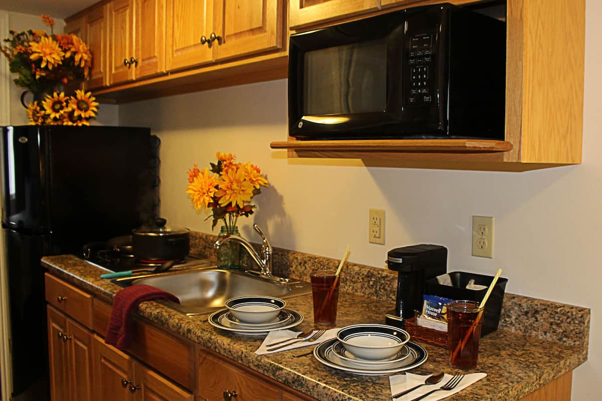 A kitchen with wooden cabinets, a black microwave, a sink, and a vase with flowers.