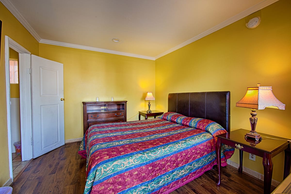 A bedroom with a bed, a nightstand, a lamp, and a door.