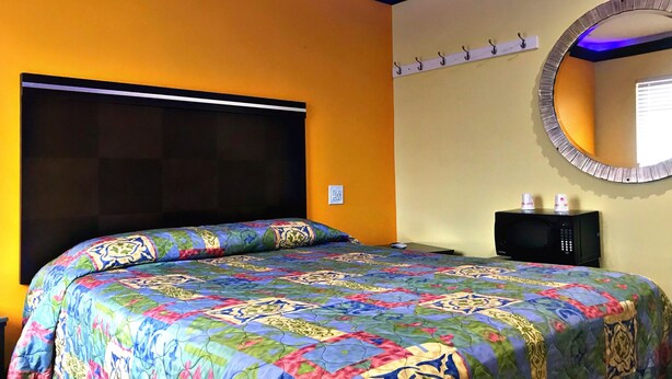 A bedroom with a large bed, a round mirror, and a small table with two cups. - Central Inn Motel (Los Angeles)