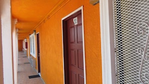 A corridor with orange walls, a brown door with the number 212, and a window with a metal grill. - Central Inn Motel (Los Angeles)
