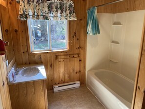 A wooden cabin bathroom with a window, a sink, and a bathtub. - Parkside Cottages and Suites (Stanhope)