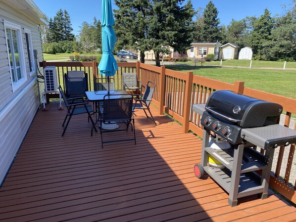 A wooden deck with a grill, outdoor table, and chairs. - Parkside Cottages and Suites (Stanhope)