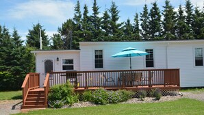 A single-story house with a wooden deck, a small porch, and a blue umbrella. - Parkside Cottages and Suites (Stanhope)