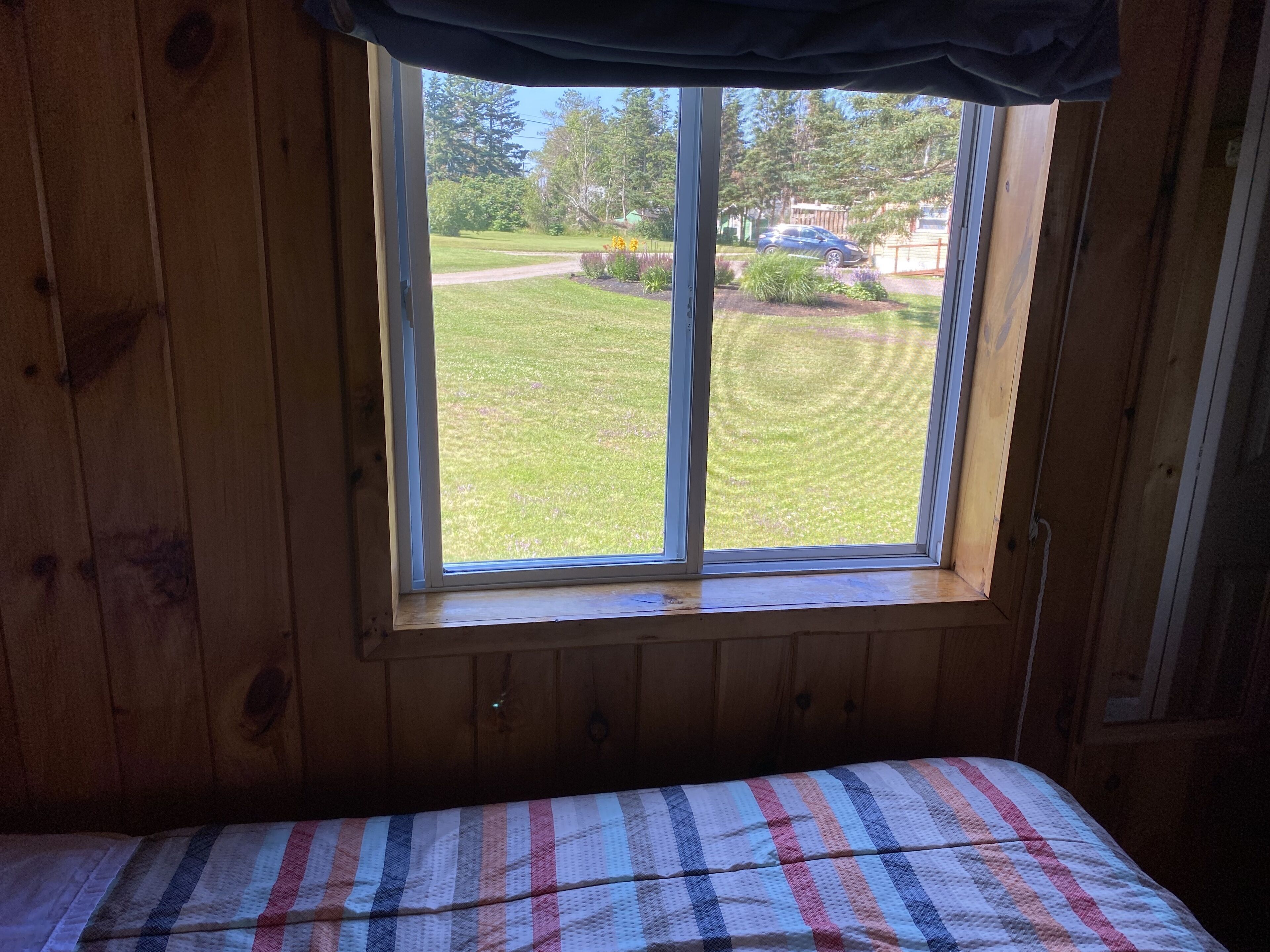 Una habitación con cama, ventana que da a un césped y un coche, y paredes de madera.