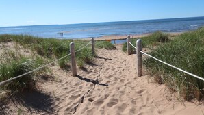 A sandy beach path leading to the ocean, bordered by grass and a rope barrier. - Parkside Cottages and Suites (Stanhope)