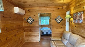 A cozy cabin interior with a wooden floor, a leather sofa, a bed with a blue curtain, and decorative wall art. - Parkside Cottages and Suites (Stanhope)