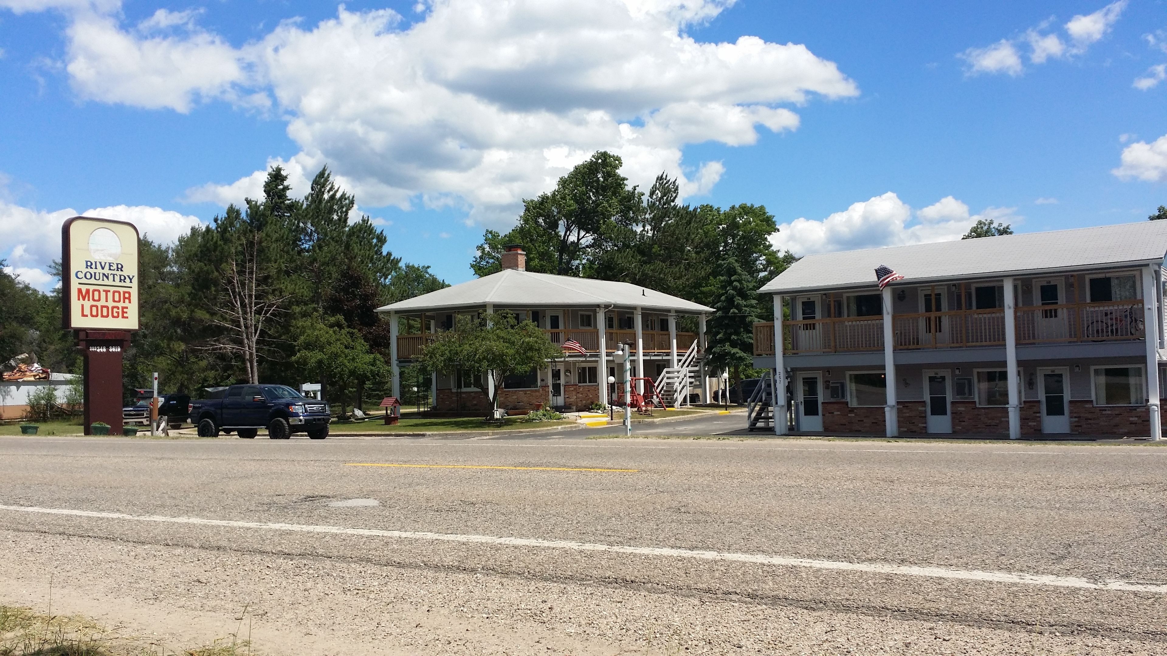 Un motel doté d’un espace extérieur abrité avec des sièges, d’un bâtiment à deux étages et d’une enseigne indiquant « River Country Motor Lodge ».