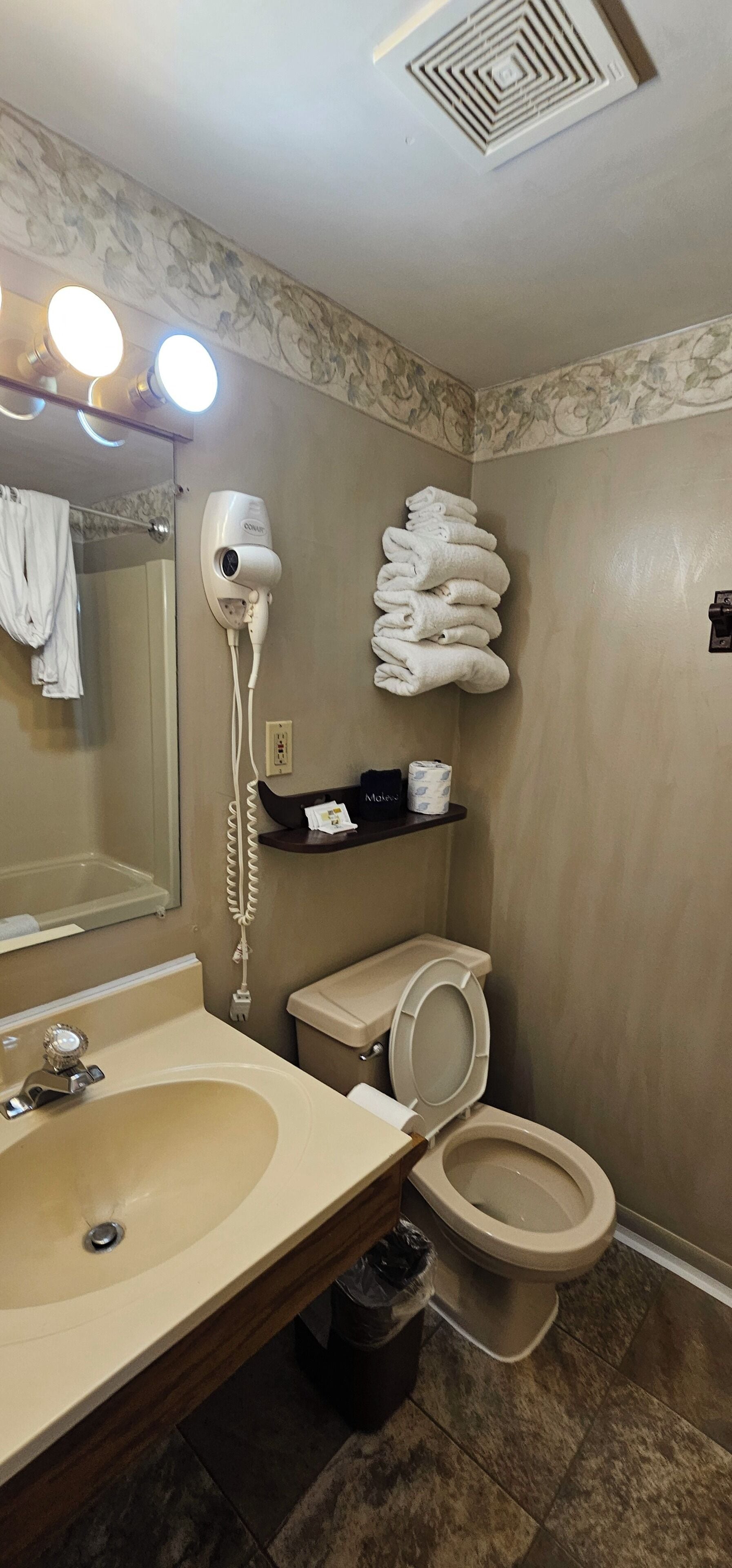 A bathroom with a sink, a toilet, a hairdryer, and a stack of towels.