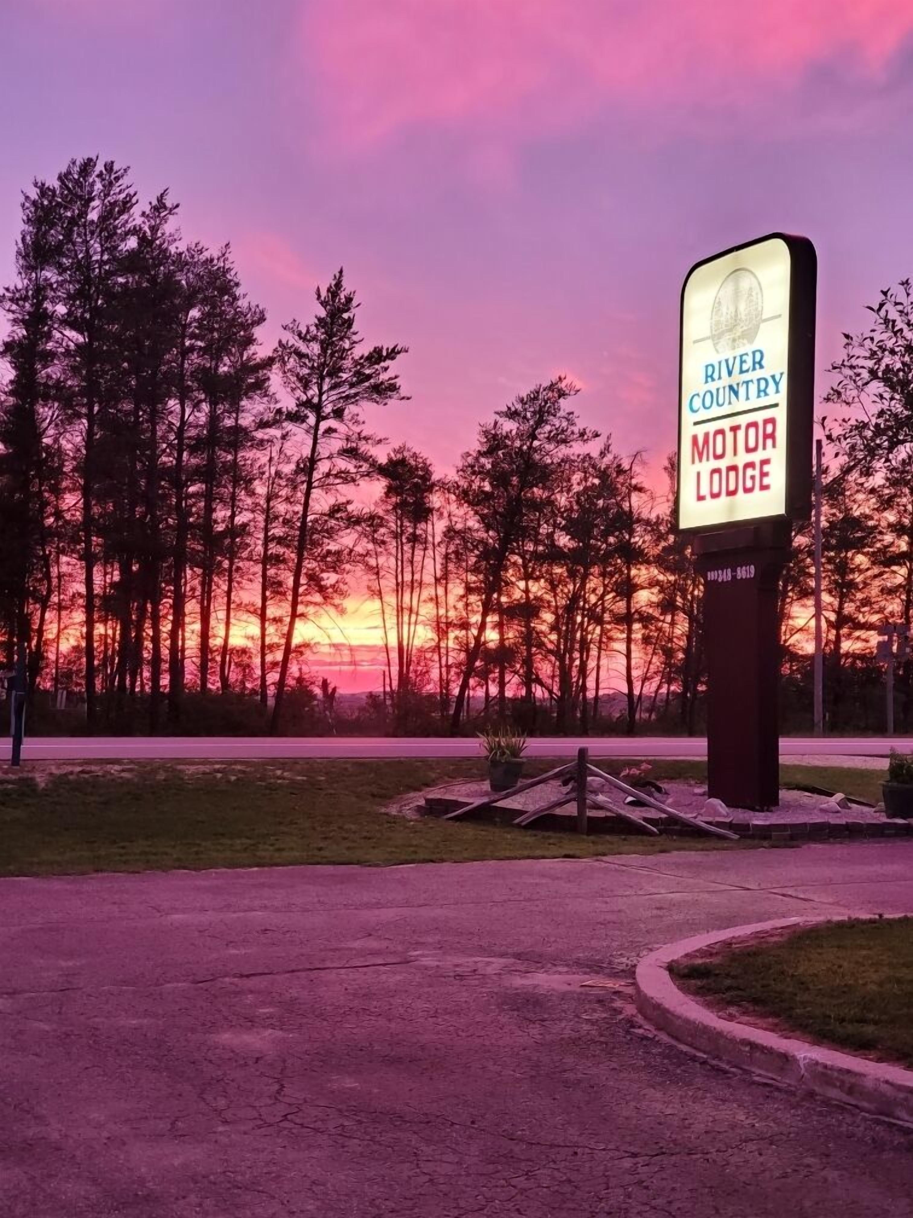 Letrero del River Country Motor Lodge con un atardecer de fondo.