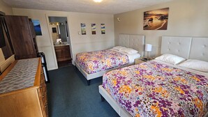 A hotel room with two beds, a wooden dresser, a vanity with a mirror, and a painting on the wall. - River Country Motor Lodge (Grayling)