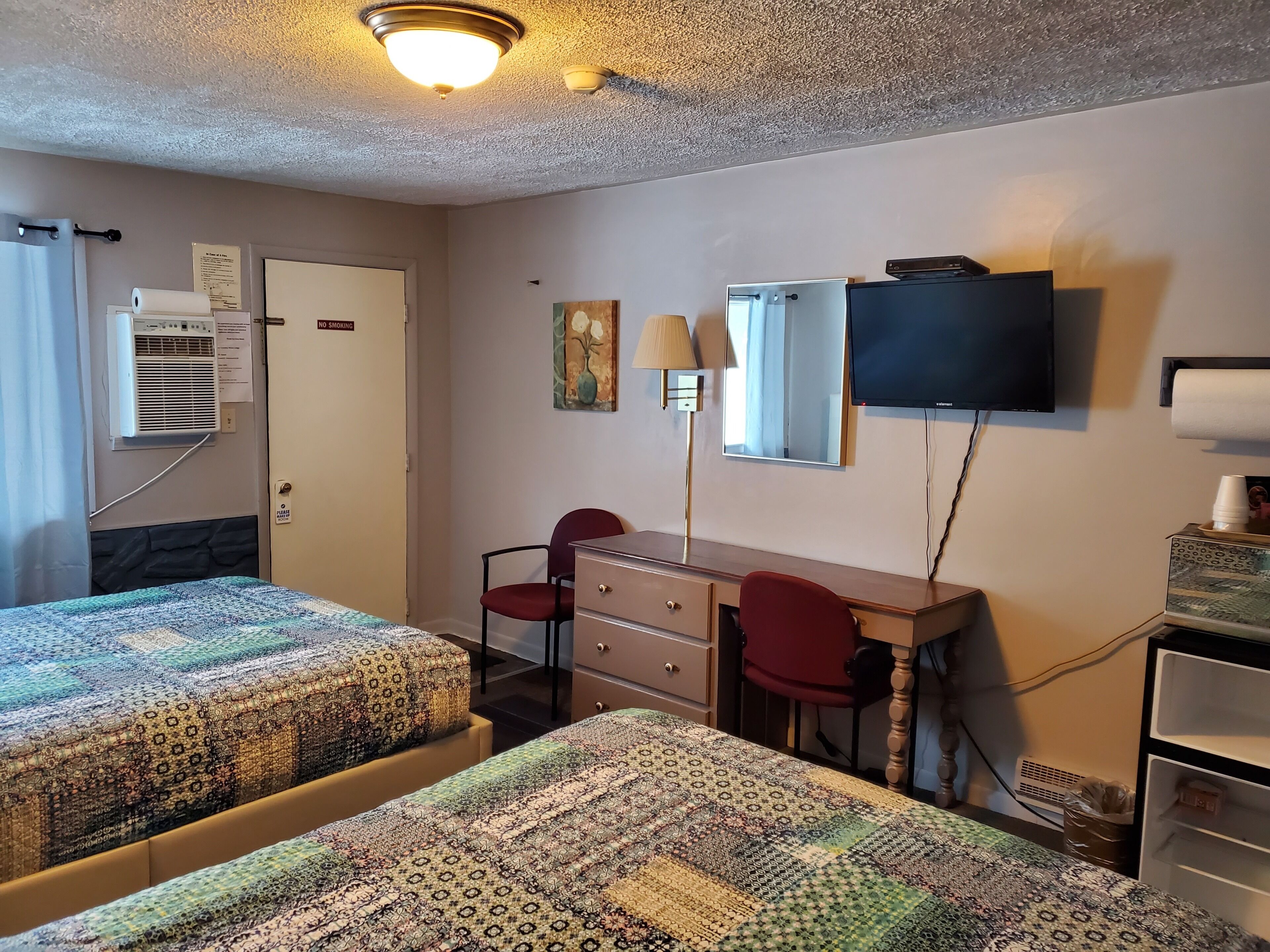 A hotel room with two beds, a desk with a chair, a television, and a mirror.