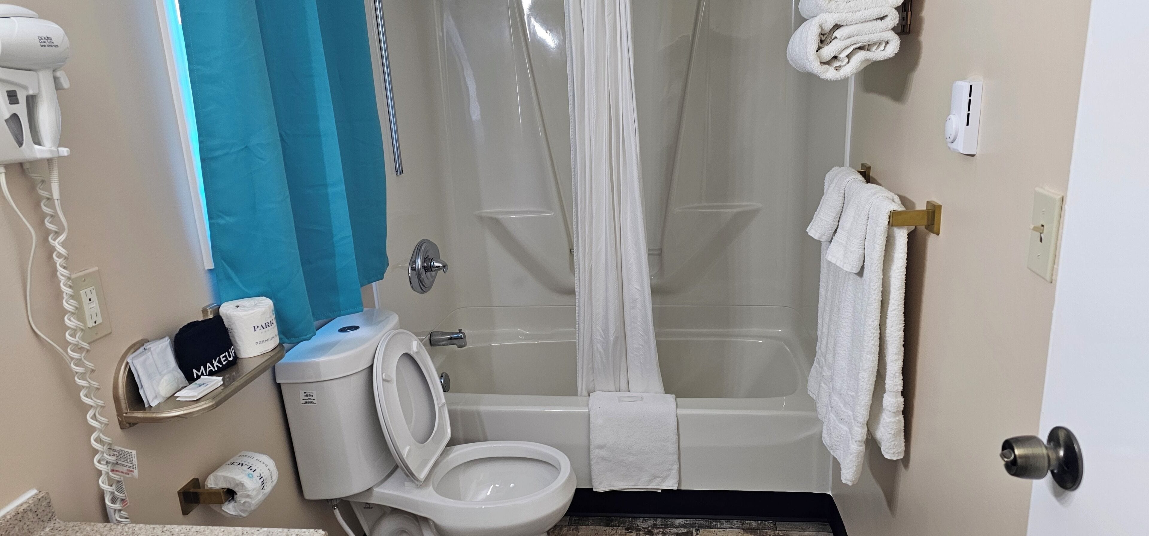 A bathroom with a toilet, shower, and bathtub. There are towels hanging on the wall and a hairdryer on the wall.