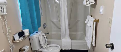 A bathroom with a toilet, shower, and bathtub. There are towels hanging on the wall and a hairdryer on the wall.
