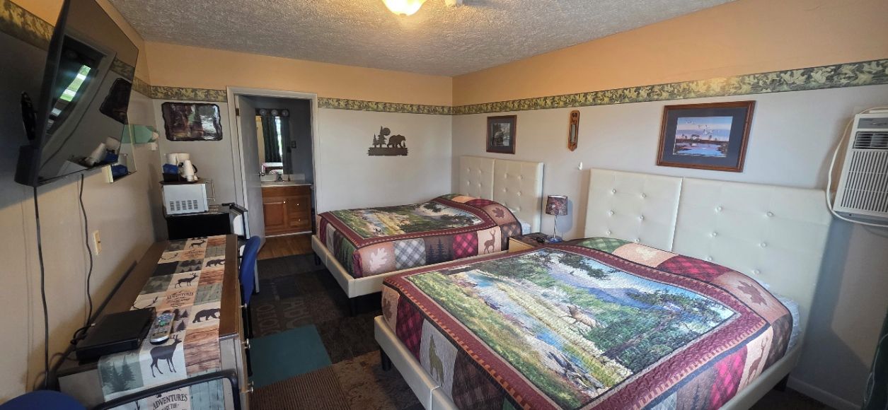 A room with two beds, a desk, a television, and a window.