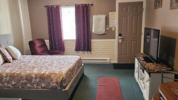A hotel room with a bed, a chair, a TV, and a desk with drawers.