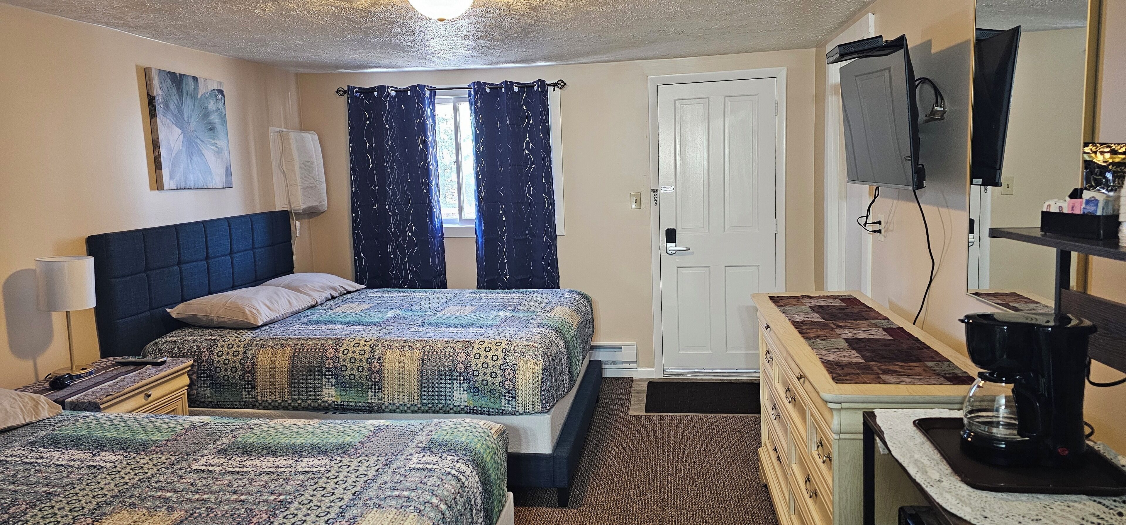 A bedroom with two beds, a desk with a coffee maker, a TV, and a door.