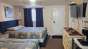 A bedroom with two beds, a desk with a coffee maker, a TV, and a door.