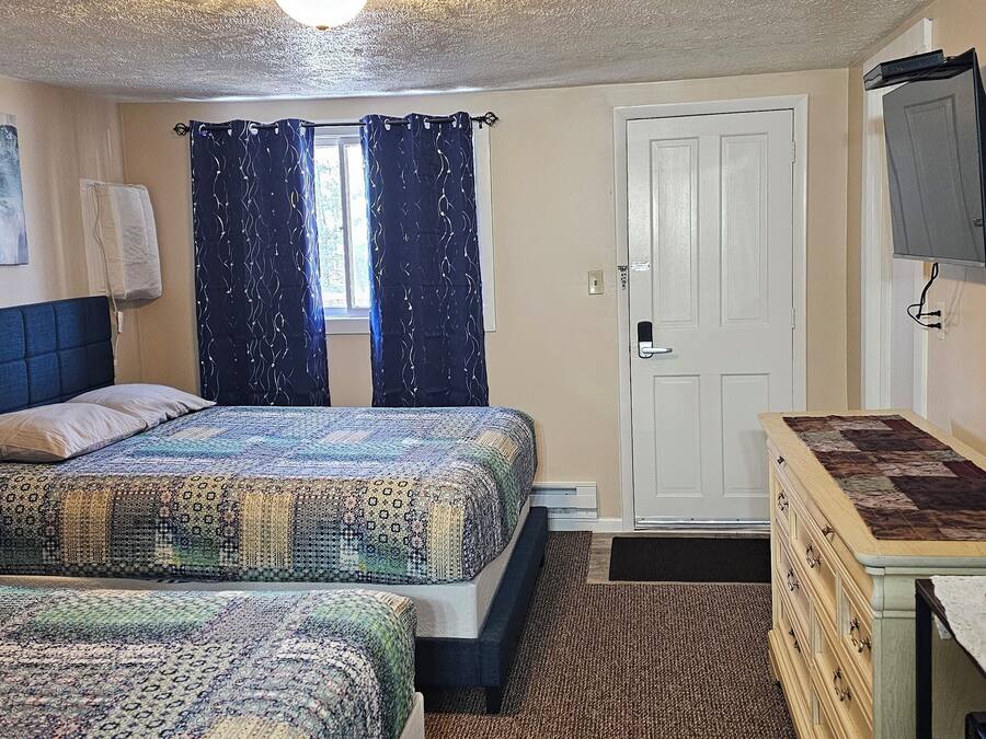 A bedroom with two beds, a desk with a coffee maker, a TV, and a door.