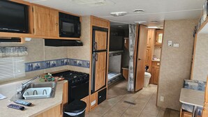 A compact RV kitchen with a stove, microwave, sink, and a small trash bin. - River Country Motor Lodge (Grayling)