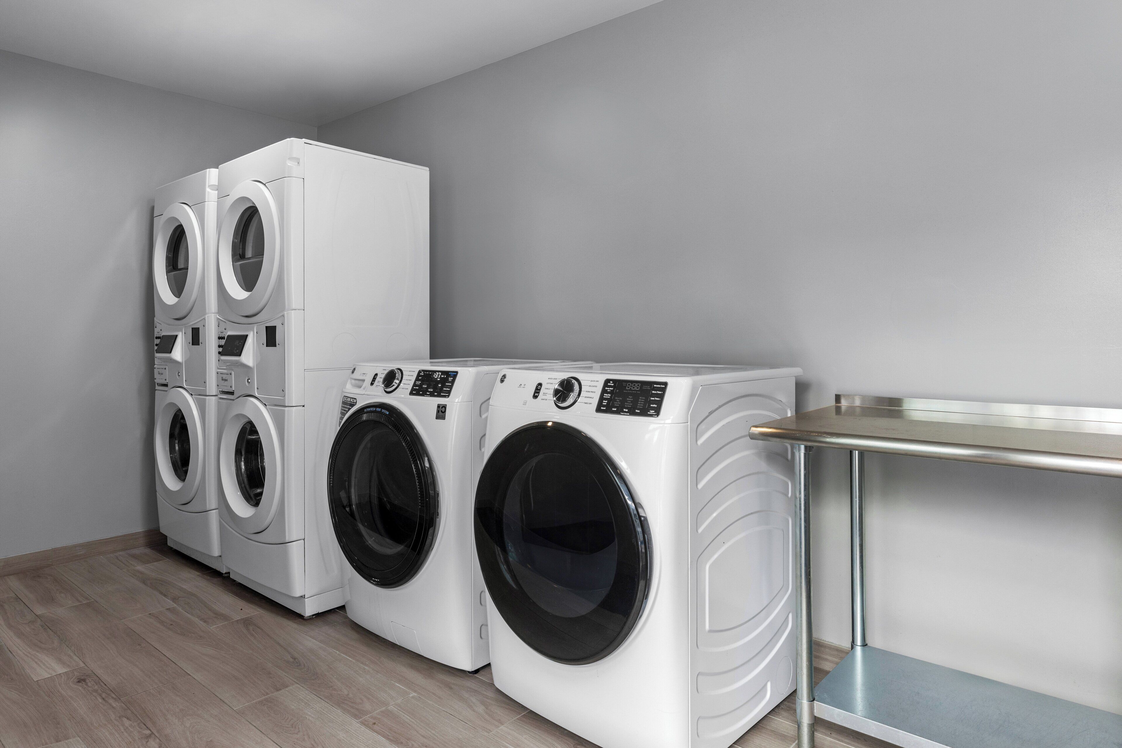 A laundry room with four white front-loading washing machines and a stainless steel table.