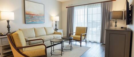 A hotel room with a sofa, armchairs, a coffee table, a TV, and a painting on the wall.