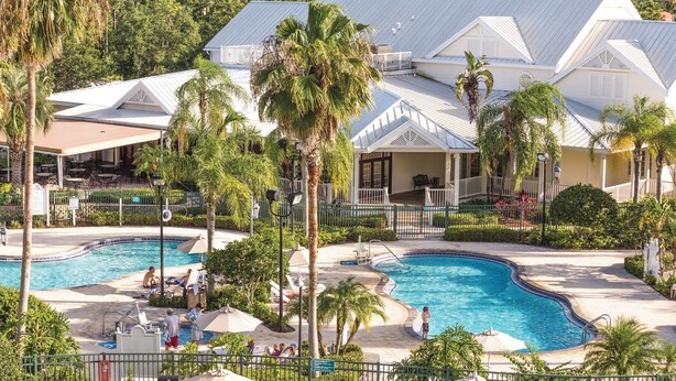 A resort with two swimming pools surrounded by palm trees and a building with a white facade and blue roof. - WorldMark Orlando - Kingstown Reef (Orlando)
