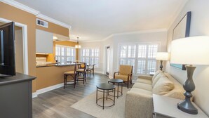 A modern living room with a sofa, a coffee table, and a TV stand. There is a kitchen area with a dining table and chairs. - WorldMark Orlando - Kingstown Reef (Orlando)