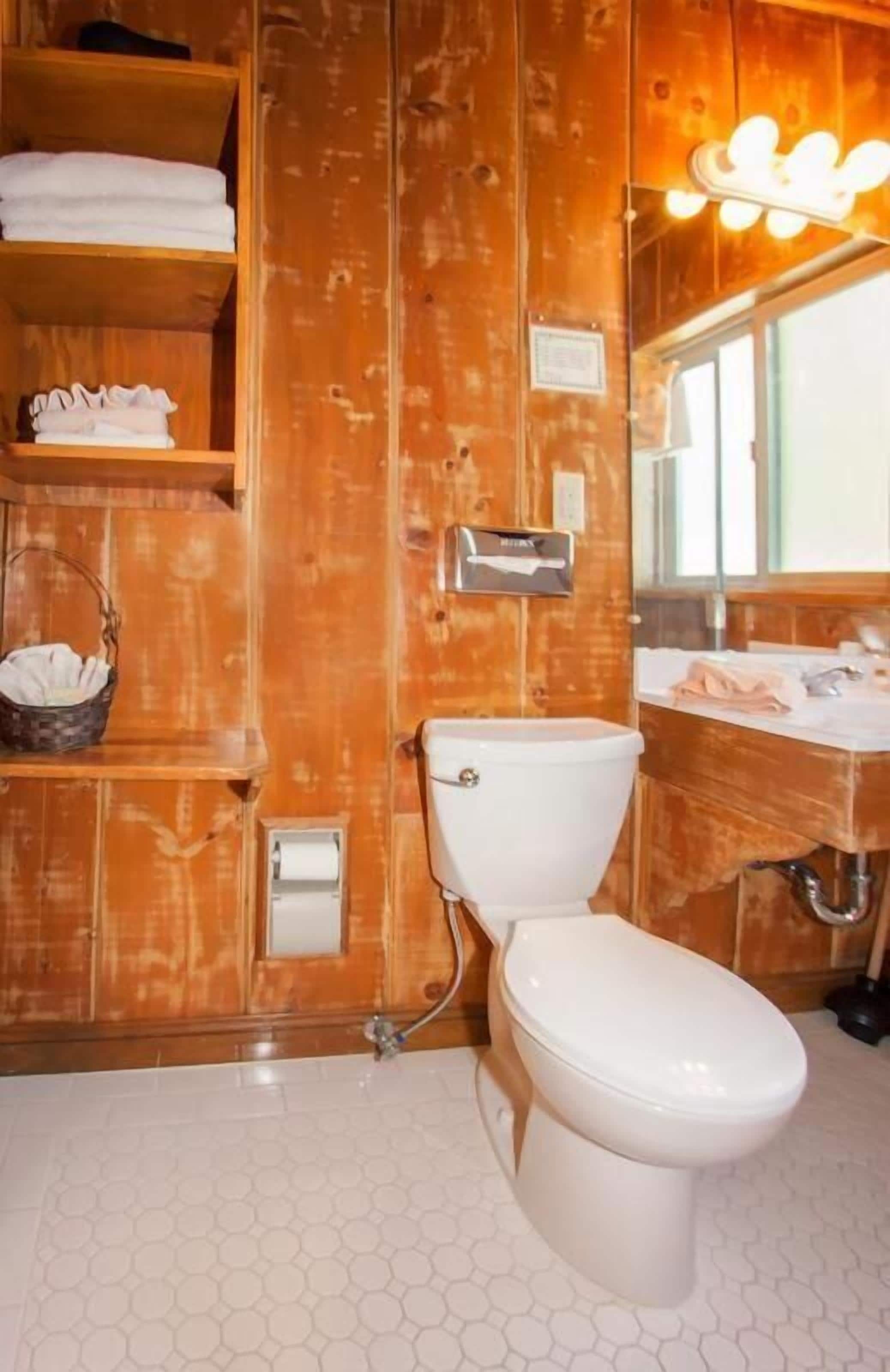 Une salle de bain aux murs lambrissés, équipée de toilettes, d’un lavabo et d’un meuble-lavabo.