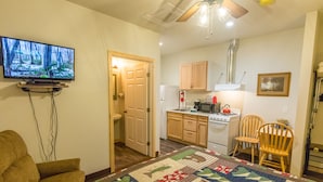 A compact living space with a television mounted on the wall, a kitchen area with wooden cabinets, a stove, and a dining area with two wooden chairs. - June Lake Motel (June Lake)