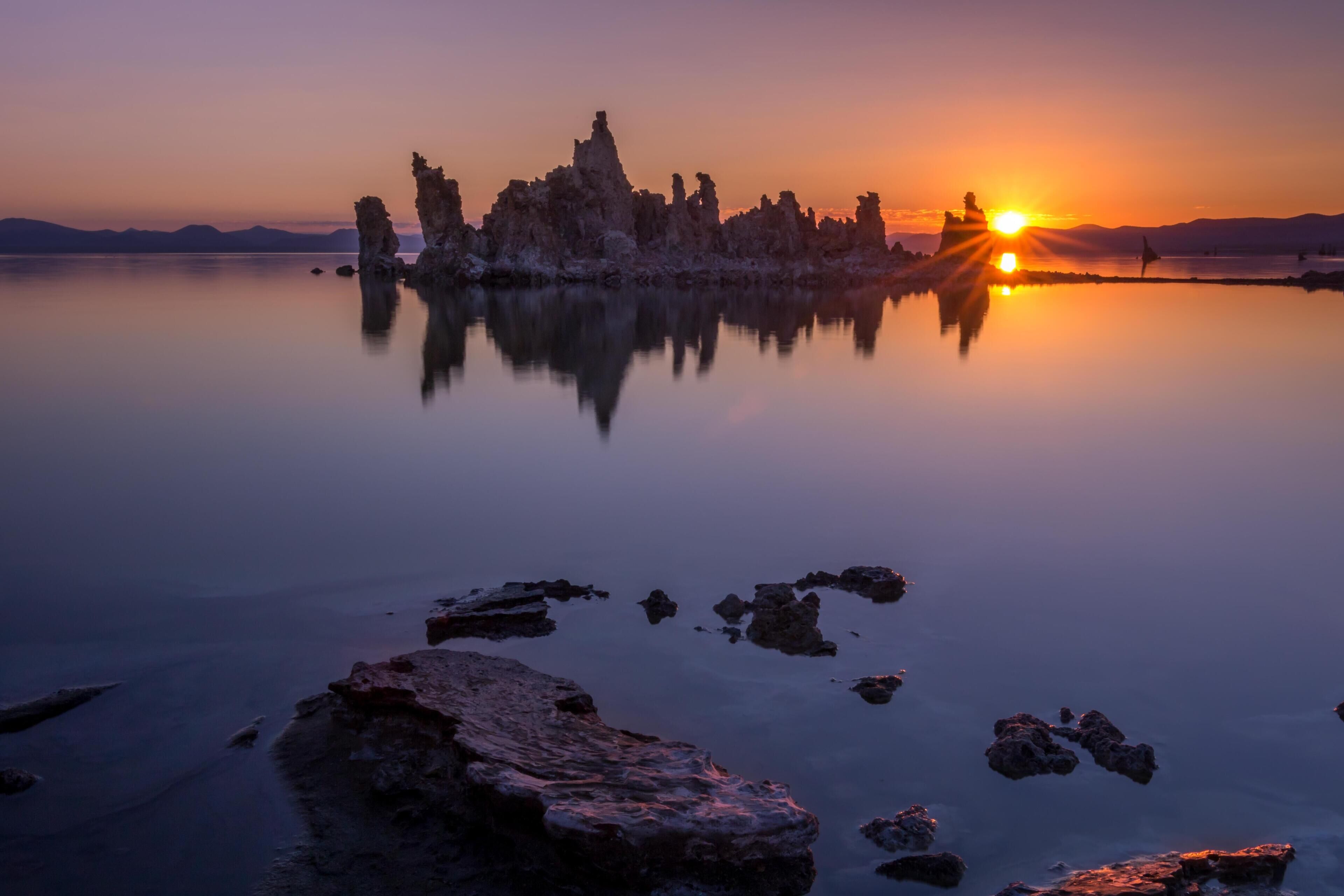 Un lago tranquilo con formaciones rocosas y un atardecer.