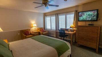 A hotel room with a bed, desk, chair, television, and a ceiling fan.