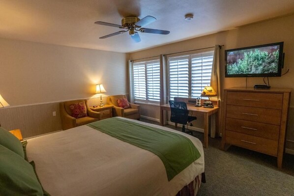 Una habitación de hotel con cama, escritorio, silla, televisor y ventilador de techo.