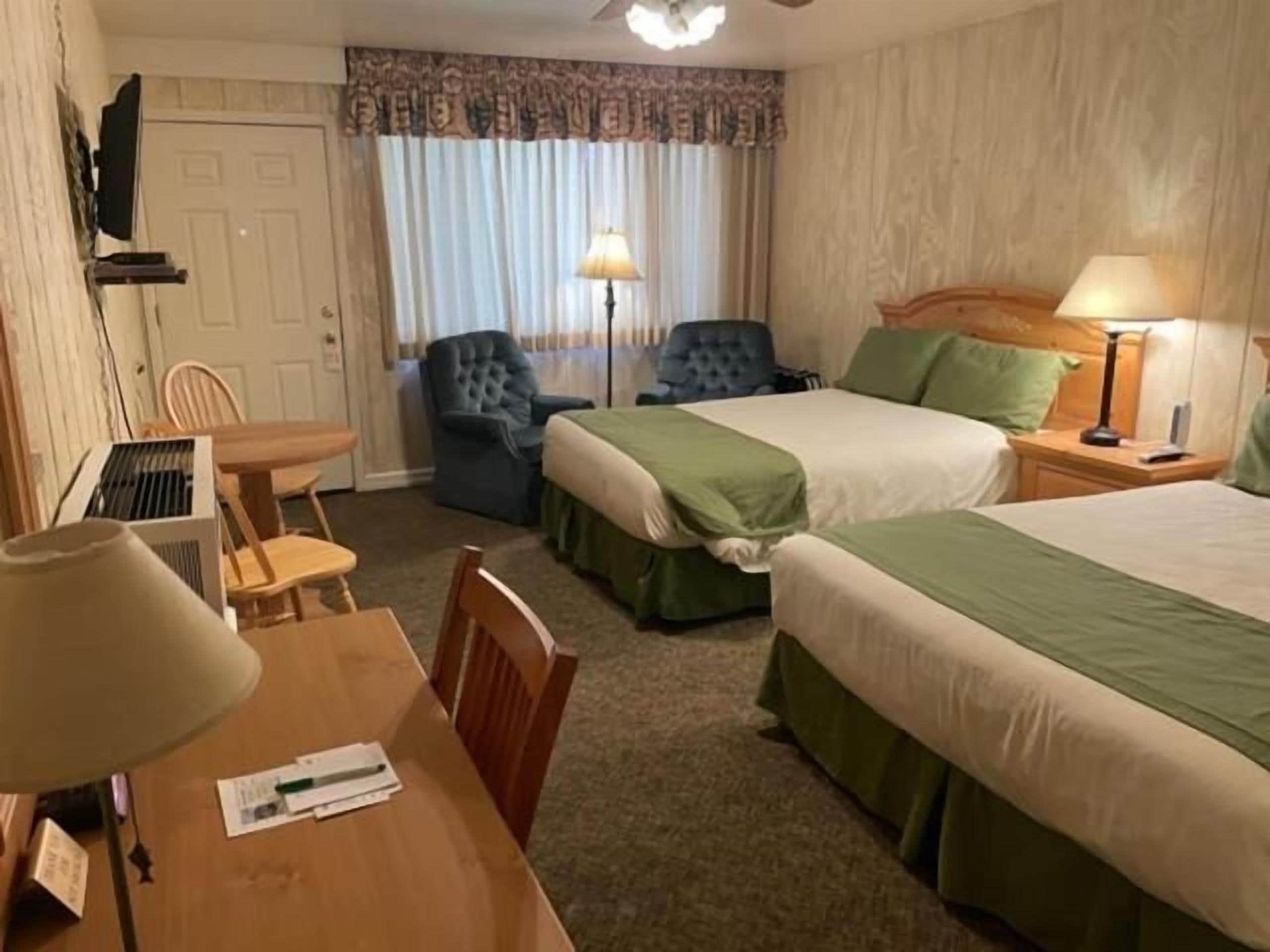 A hotel room with two beds, a desk, a chair, a TV, and a window with curtains.