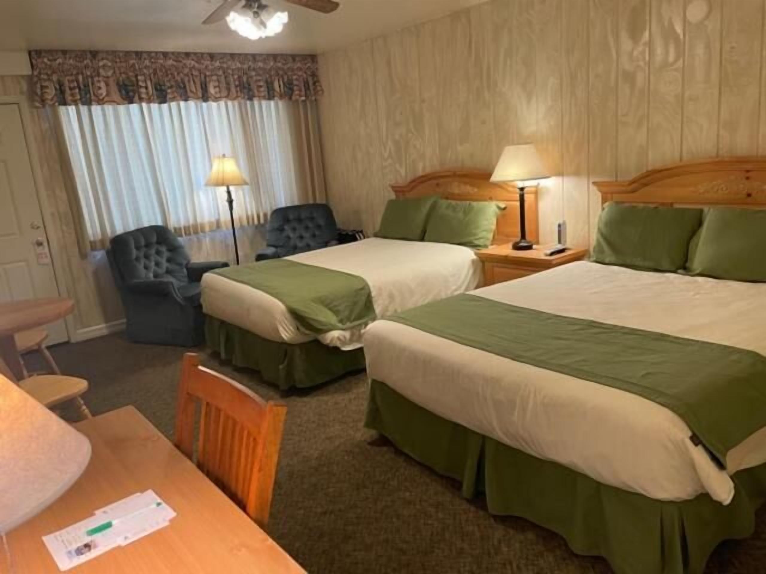 A hotel room with two beds, a desk, a chair, and a lamp.