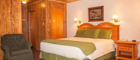 A wooden-paneled room with a bed, a chair, a nightstand, and a lamp.