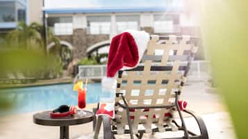 A poolside chair with a red and white blanket, a drink with a straw, and headphones on a small table.