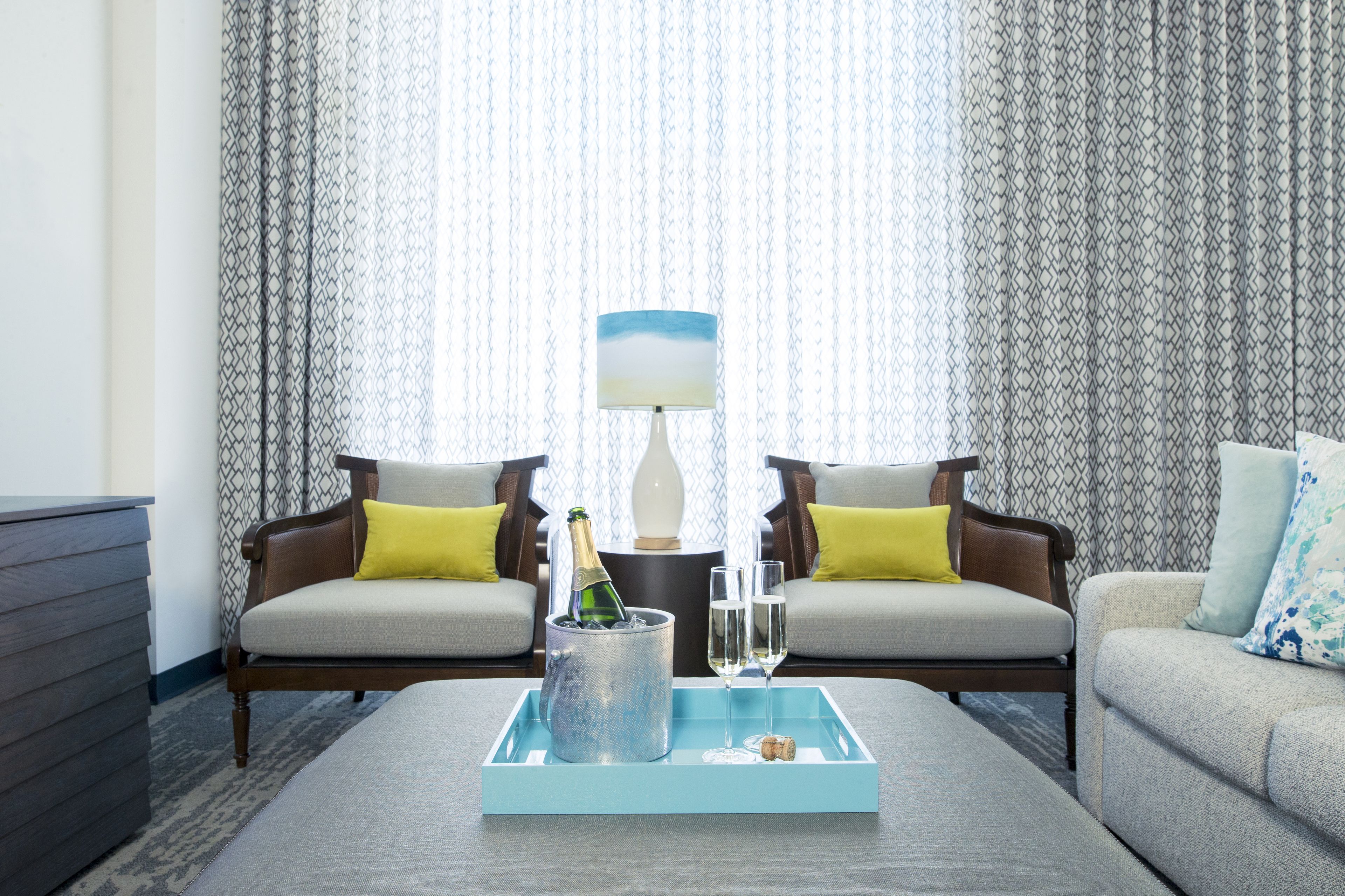 A living room with a sofa, two armchairs, a coffee table with a tray, a lamp, and a bottle of champagne.