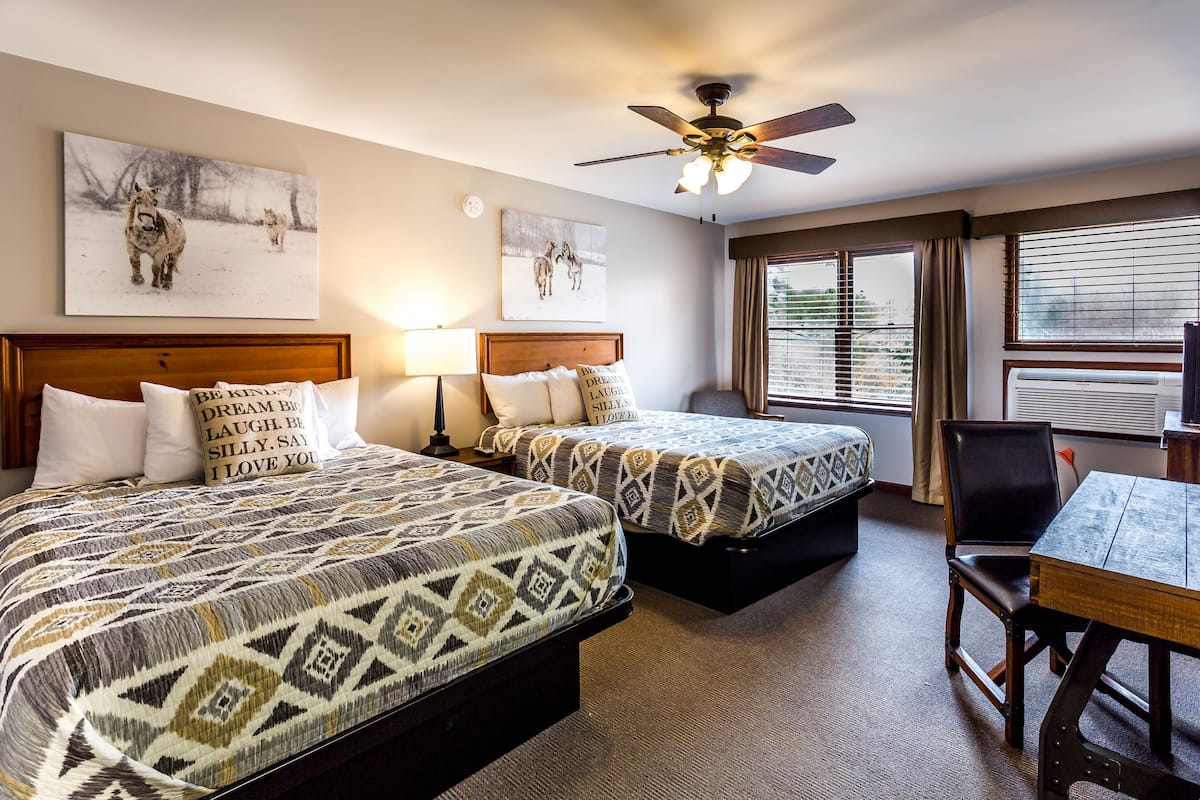 A hotel room with two beds, a ceiling fan, and a dining table.