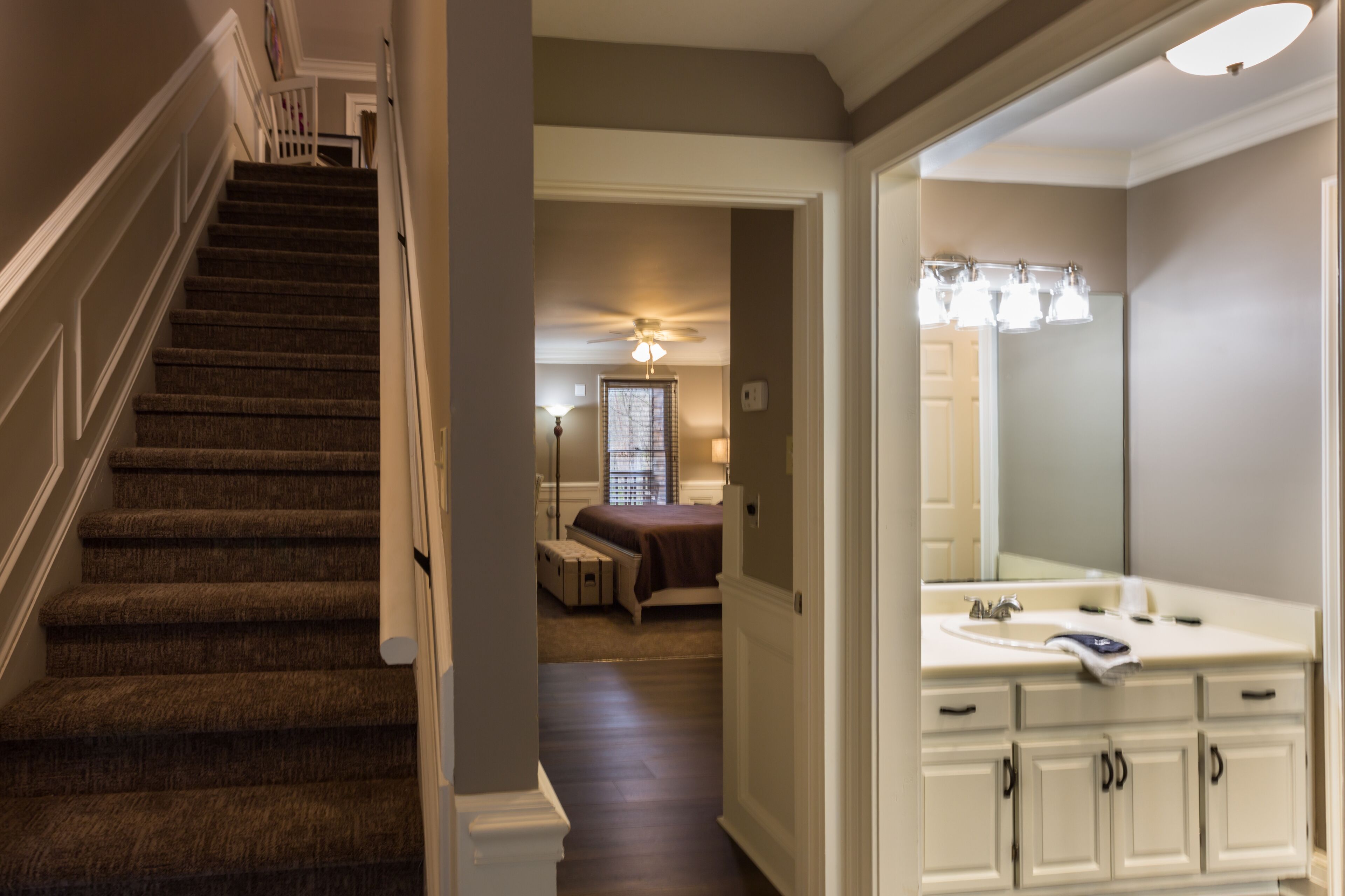 A staircase leading to a bedroom with a large bed and a window. There is a bathroom with a mirror and a sink.