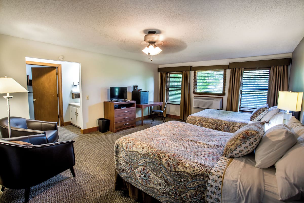 A hotel room with two beds, a desk, a chair, a television, and a ceiling fan.