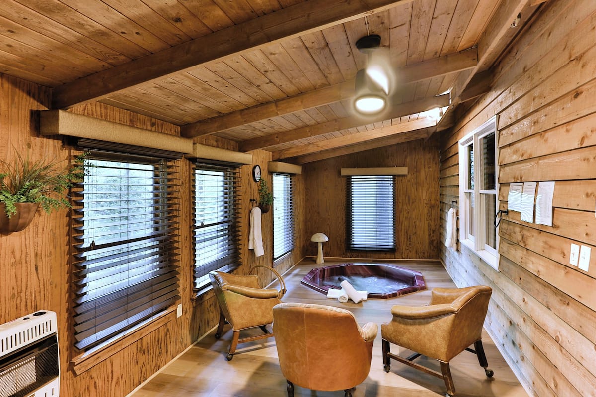 A wooden cabin interior with a hot tub, two armchairs, and a ceiling light.