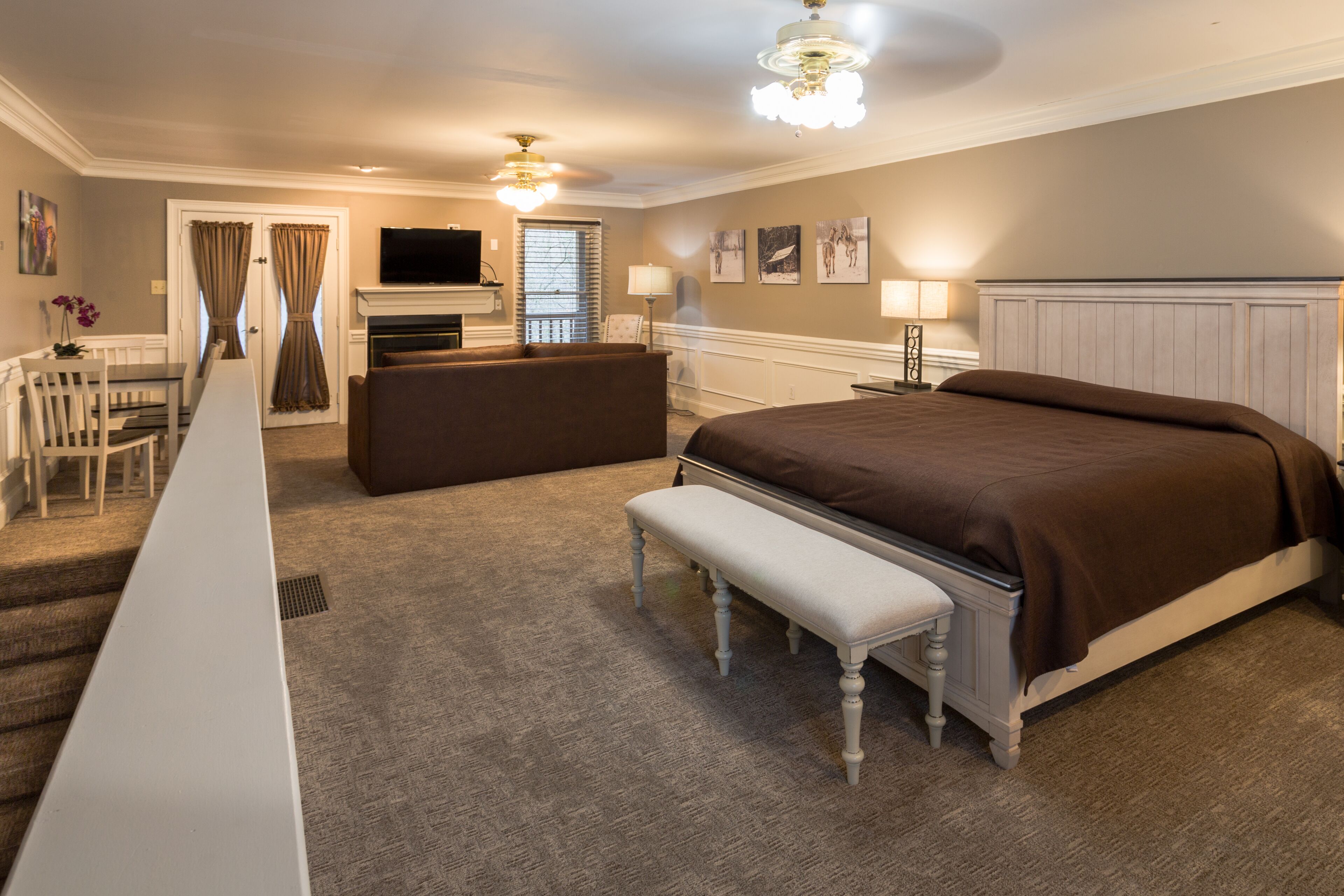 A hotel room with a large bed, a bench, a desk, a television, and a fireplace.