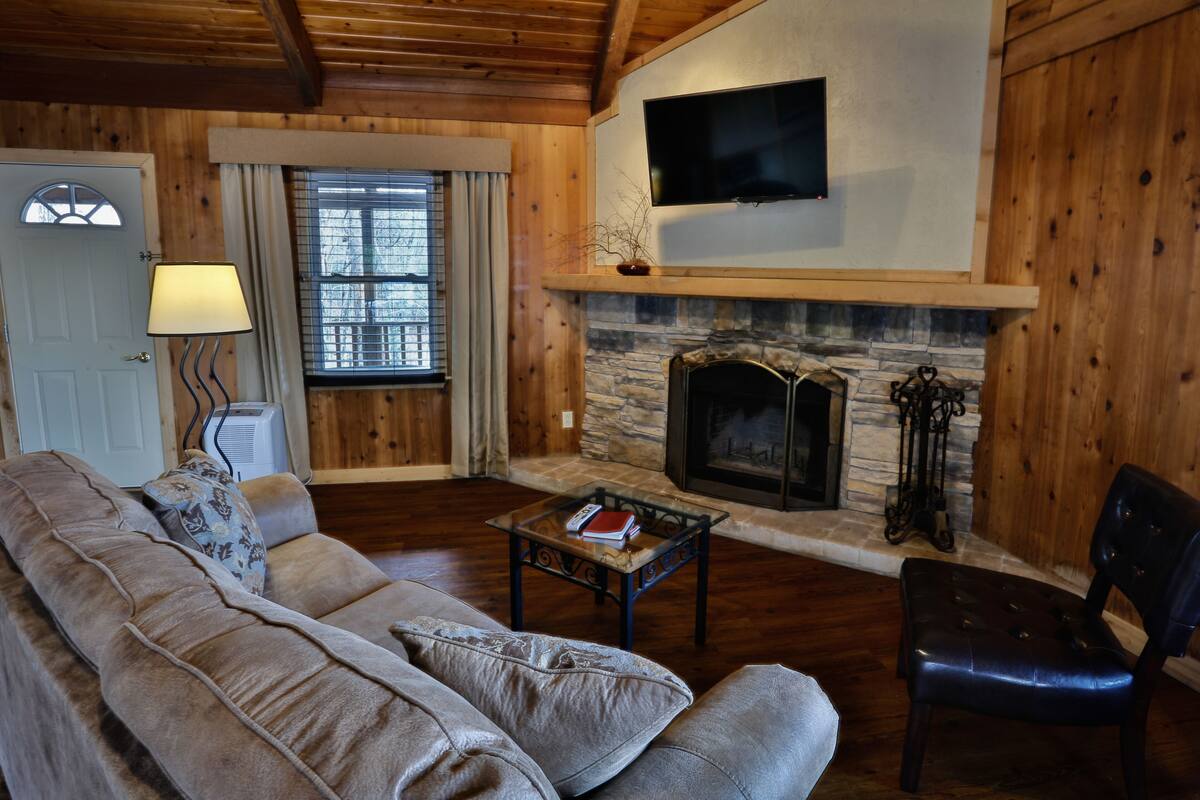 A cozy living room with a stone fireplace, a sofa, a chair, and a television mounted on the wall.
