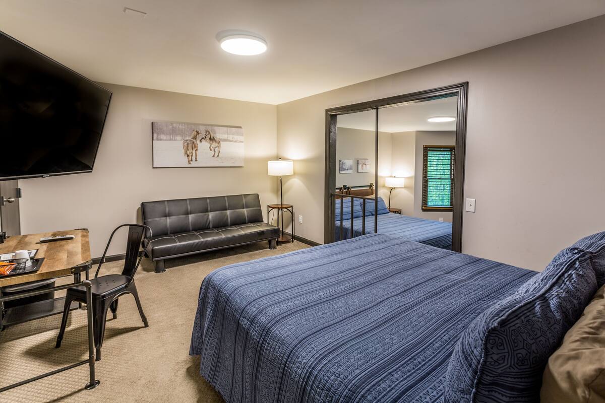 A hotel room with a bed, a desk with a chair, a sofa, a TV, and a mirror.
