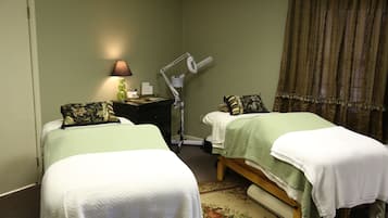 Two single beds with green bedspreads and white comforters, a nightstand with a lamp, and a small table between them.