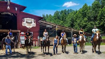 A group of people on horseback in front of a building with a sign reading "Gold City Horseback Riding & Western Outfitters."