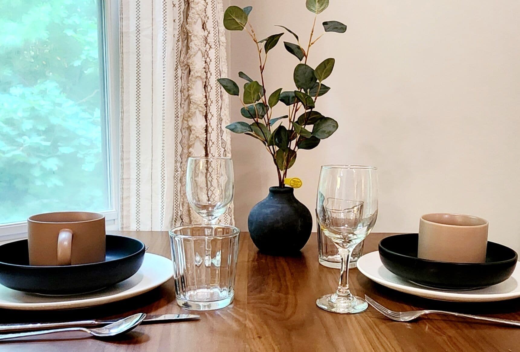 A dining table set with plates, bowls, glasses, and a vase with a plant.