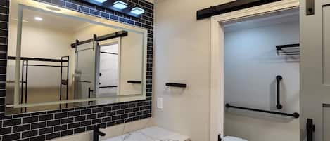 A bathroom with a black tiled backsplash, a white sink, a large mirror, and a white toilet.